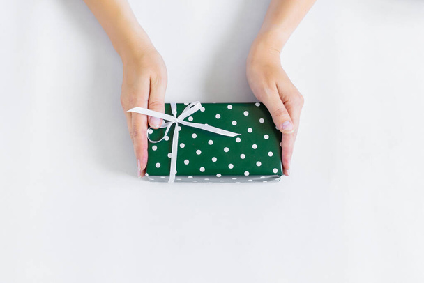 Handen hebben een geschenk in groene verpakking. - Foto, afbeelding