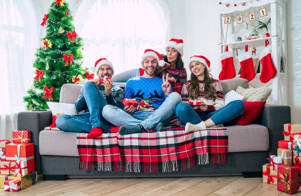 Merry Christmas and Happy New Year. The big happy excited group of young friends in Christmas santa hats with gift boxes are having fun together while sitting on the couch. - Φωτογραφία, εικόνα
