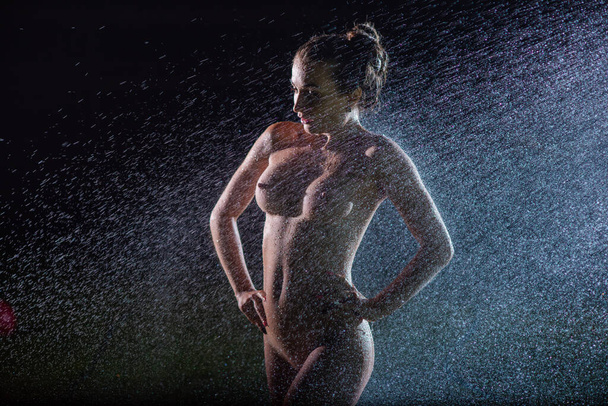 A beautiful European nude woman under sprinkler at night - Foto, Imagen