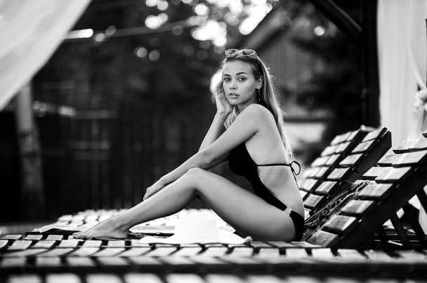 Beautiful girl in a black swimsuit on a wooden lounger - Φωτογραφία, εικόνα