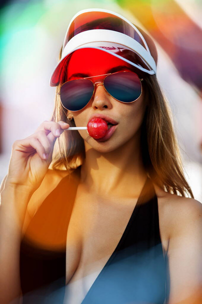 Portrait of beautiful woman in sun visor with lollipop - Фото, изображение