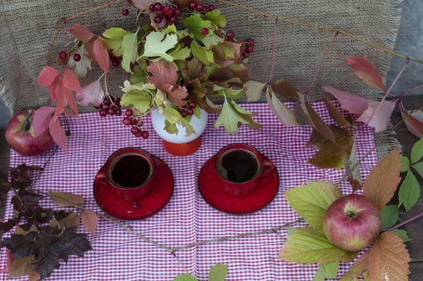 Kilátás fentről. Egy rózsaszín kockás szalvétán van két csésze kávé, egy csokor vibráló ág, alma és őszi levelek. - Fotó, kép