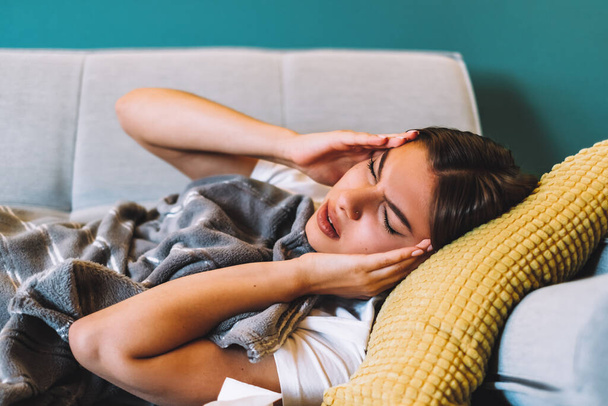 Cansada jovem fêmea tocando na testa com dor de cabeça enxaqueca ou febre, deitada em um sofá na sala de estar. .. Foto de alta qualidade - Foto, Imagem