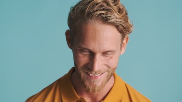 jong blond baardman glimlachen en likken lip op camera over kleurrijke achtergrond - Video