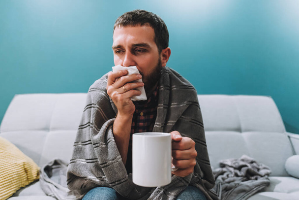 Sick young man blowing her nose using facial tissues and holding white mug - Foto, afbeelding