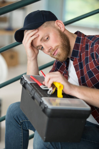 worried tradesman sat on stairs holding his toolbox - Foto, immagini