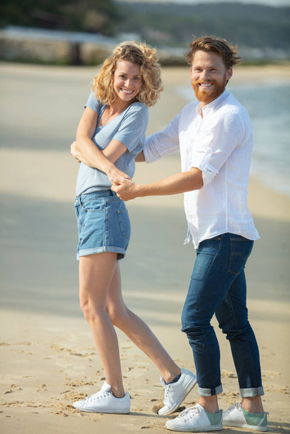 relaxed couple holding hands and slowly walking along water shore - Foto, Imagem