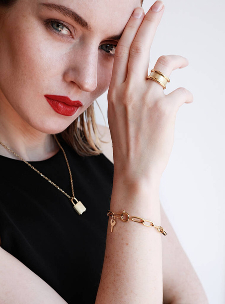 Close-up portrait of beautiful woman with red lips and golden jewellery posing over white wall background. Vertical. - Fotó, kép