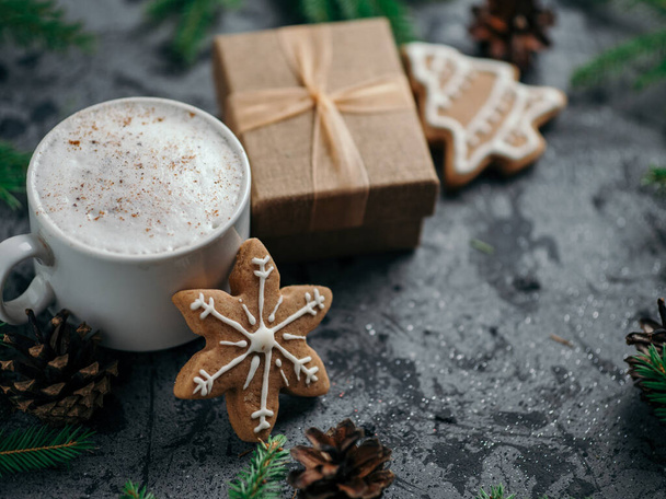 Χριστουγεννιάτικος καφές καπουτσίνο στο τραπέζι με ασημένιες γυαλιστερές μπάλες, κλαδιά χριστουγεννιάτικου δέντρου και σπιτικά μπισκότα τζίντζερ - Φωτογραφία, εικόνα