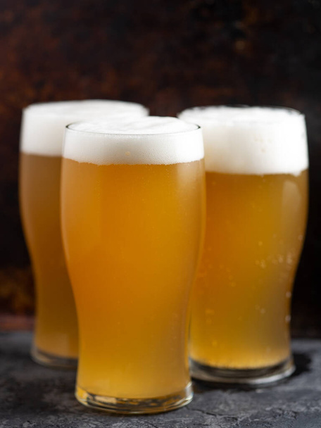 drei Gläser helles, ungefiltertes Bier in Nahaufnahme auf dunklem Hintergrund - Foto, Bild