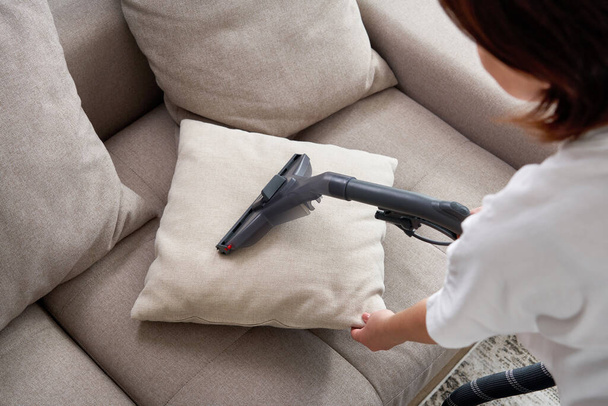 Young housewife Cleaning Sofa with Vacuum Cleaner in living room - Fotoğraf, Görsel