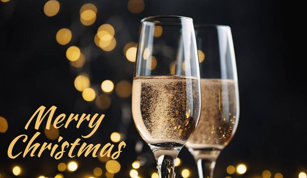 Vrolijk kerstfeest. Twee glazen champagne op een donkere achtergrond met bokeh bloemenslingers - Foto, afbeelding