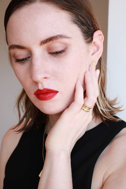 Close-up portrait of beautiful young woman with red lips and golden jewellery posing over white wall background. - Fotografie, Obrázek