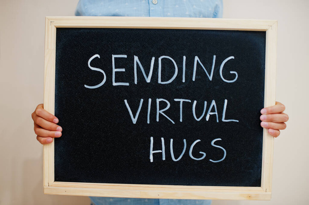 Sending virtual hugs. Coronavirus concept. Boy hold inscription on the board. - Foto, imagen
