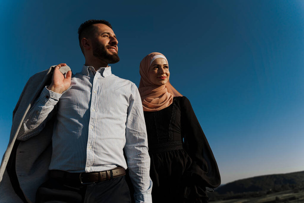 Muzułmańska historia miłosna na tle błękitnego nieba. Wesołe mieszane uśmiechy i uściski. Kobieta ubrana w hidżab patrzy na swojego mężczyznę. Ogłoszenie dla agencji randkowej online - Zdjęcie, obraz