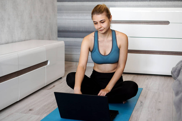 Дівчина тренується вдома і дивиться відео на ноутбук, тренування у вітальні
 - Фото, зображення