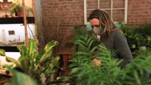 Γυναίκα φορώντας μάσκα κοιτάζοντας τα φυτά στο κατάστημα - Πλάνα, βίντεο