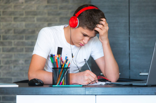 Un chico con audífonos hace deberes, escucha la lección. Hogar, educación a distancia, autoeducación de los niños. - Foto, imagen