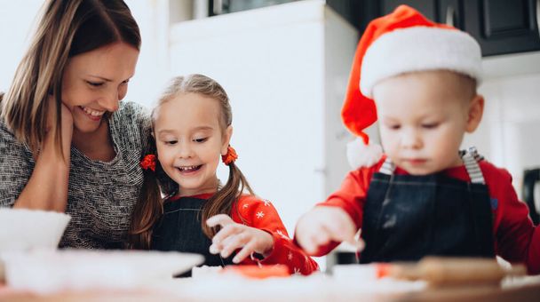 Valkoihoinen äiti ja hänen lapsensa pukeutunut joulupukki vaatteita ruoanlaitto ja leivonta evästeet joulu - Valokuva, kuva