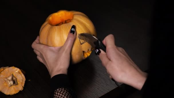 Young woman prepares a pumpkin for Halloween. Cuts out the eyes. Celebration - 映像、動画