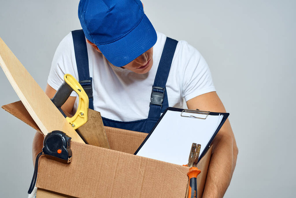 άνθρωπος με στολή εργασίας με ένα κουτί στα χέρια του εργαλεία φορτωτή παράδοση φως φόντο - Φωτογραφία, εικόνα