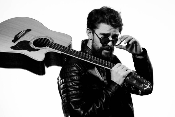 Um homem segura uma guitarra em suas mãos emoções musicais jaqueta de couro preto óculos escuros estúdio luz fundo - Foto, Imagem