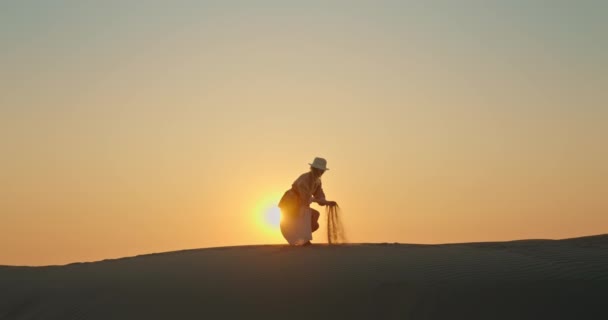 Mujer feliz con arena soplando por el viento con puesta de sol dorada en el fondo - Metraje, vídeo