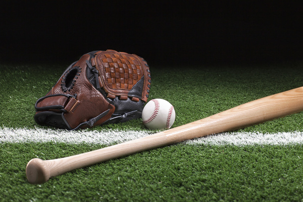 Baseball with mitt and bat on green grass at night - Фото, зображення