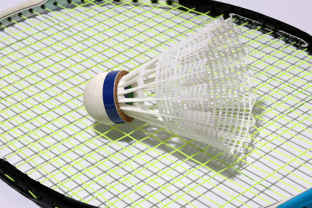 Plastikowy wahadłowiec badmintona założony na zielony plastikowy wahadłowiec badmintona założony na zieloną sieć rakiety badmintona. jest korkiem, do którego przymocowane są pióra tworzące kształt stożka. - Zdjęcie, obraz