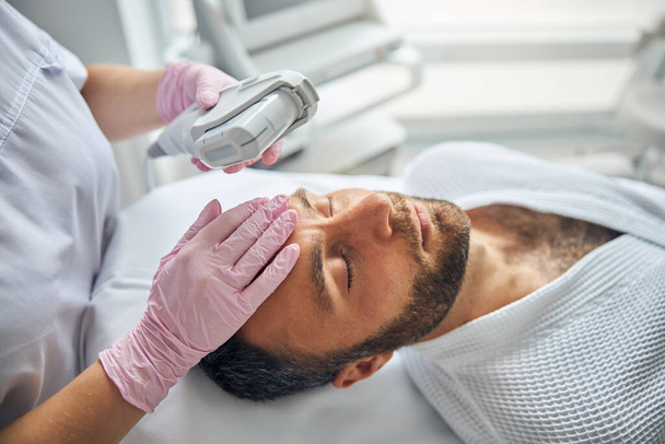 Beau jeune homme recevant un traitement facial au laser dans une clinique cosmétologique - Photo, image