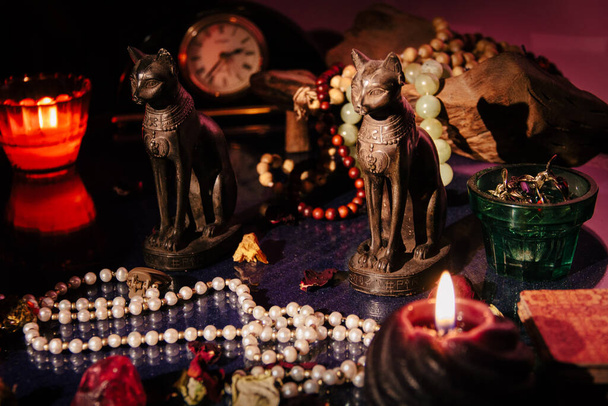 Mystical table with occult attributes. Stone rosaries, candles, antique clock, ancient Egypt figurines of cats - Photo, Image