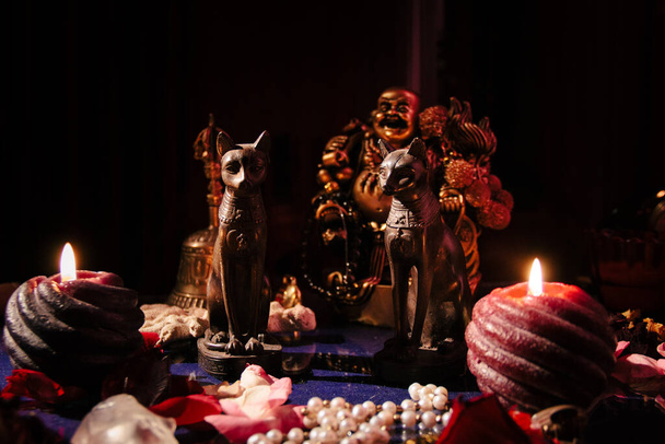 Tavolo con simboli mistici. Statuetta di Buddha, candele, rosario in pietra, statuette di gatti dell'antico Egitto. - Foto, immagini