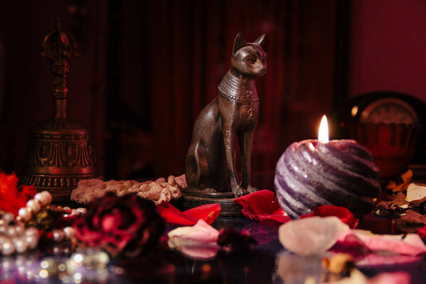 Mystische Tabelle mit okkulten Attributen. Steinerne Rosenkränze, Kerzen, antike Uhr, Katzenfiguren aus dem alten Ägypten - Foto, Bild