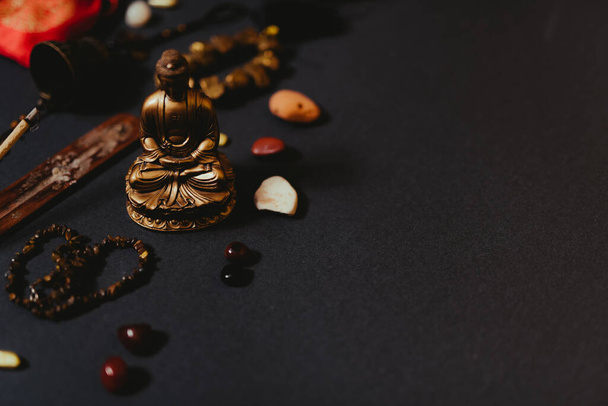 Okultní symboly umístěné na černém pozadí. Aroma tyčinka, Buddhova figurka, kamenný růženec. Horní pohled - Fotografie, Obrázek