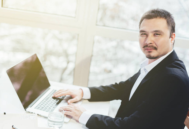 アジアの成功したビジネスマンはノートパソコンでテーブルに座っている。ウィンドウの背景. - 写真・画像