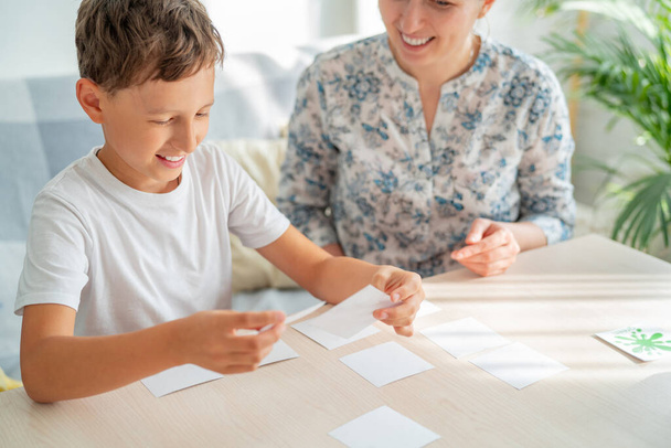 7-jarige jongen speelt een geheugenbordspel met zijn moeder om thuis geheugen en aandacht te ontwikkelen. Het kind speelt met de flash cards, leuk om tijd door te brengen met mijn moeder. Kleuren en taal leren. - Foto, afbeelding