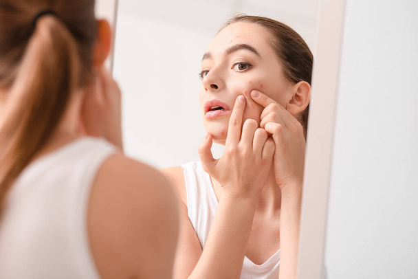 Young woman with acne problem squishing pimples near mirror - Photo, Image