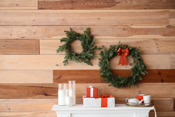 Hermosas coronas de Navidad colgando en la pared cerca de la chimenea en la habitación - Foto, Imagen