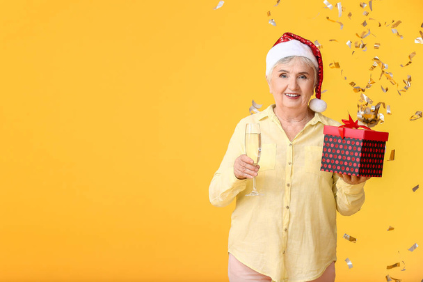 Elderly woman with Christmas gift and champagne on color background - Photo, Image