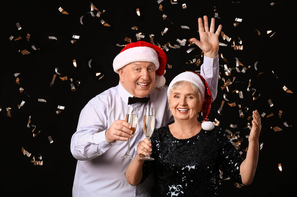 Ηλικιωμένο ζευγάρι με σαμπάνια γιορτάζει τα Χριστούγεννα σε σκούρο φόντο - Φωτογραφία, εικόνα