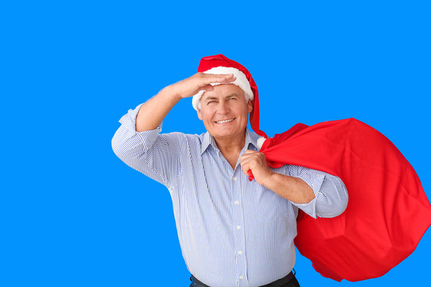 Elderly man in Santa hat and with bag on color background - Photo, Image