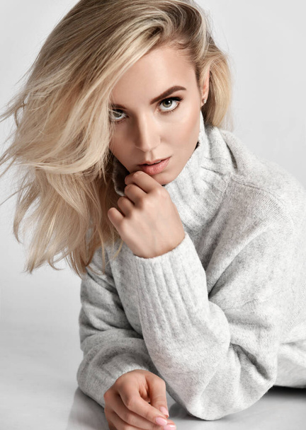 Portrait of young sexy flirting blonde woman vamp in warm knitted sweater looking at camera touching her lips - Фото, изображение