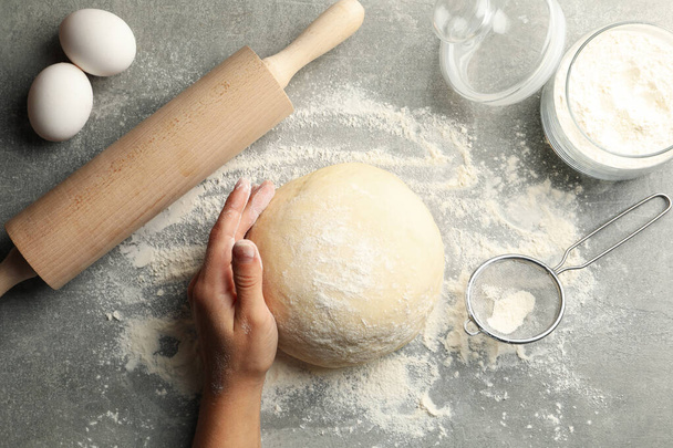 Female hand hold dough on gray background with ingredients for baking - Φωτογραφία, εικόνα