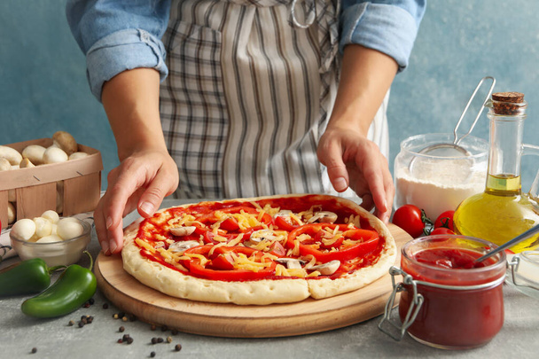 Donna tenere pizza cruda su sfondo grigio con ingredienti per la cottura - Foto, immagini