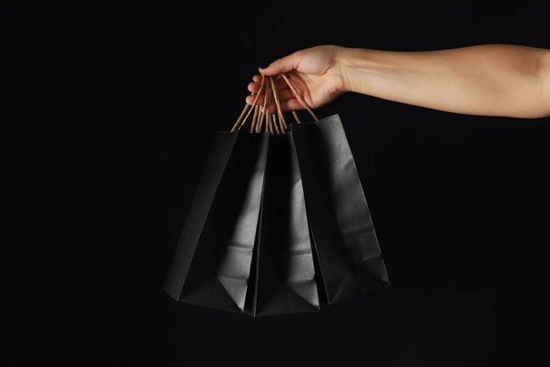 Vrouwelijke handvat papieren zakken op zwarte achtergrond - Foto, afbeelding
