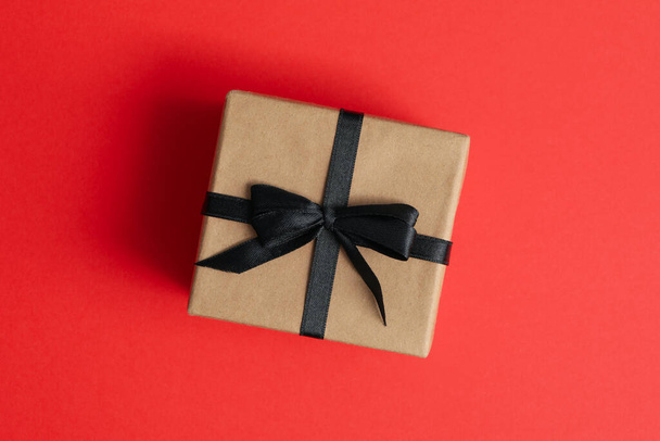 Κουτί δώρου με μαύρο φιόγκο σε κόκκινο φόντο - Φωτογραφία, εικόνα