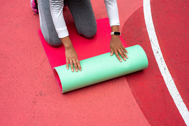 A fiatal nő kezével zöld szőnyeget terít térdelés közben. - Fotó, kép