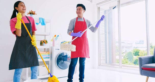 Οι σύζυγοι διασκεδάζουν ενώ καθαρίζουν το δωμάτιό τους. Ευτυχισμένο ζευγάρι Ασιατών που περνούν χρόνο μαζί στο σπίτι. - Φωτογραφία, εικόνα