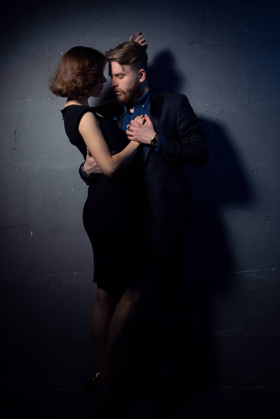 A brutal bearded man in a suit gently hugs an elegant woman in a black evening dress - Foto, afbeelding