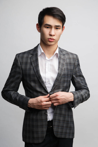 Young asian man in stylish checkered jacket isolated on gray background. - Photo, image